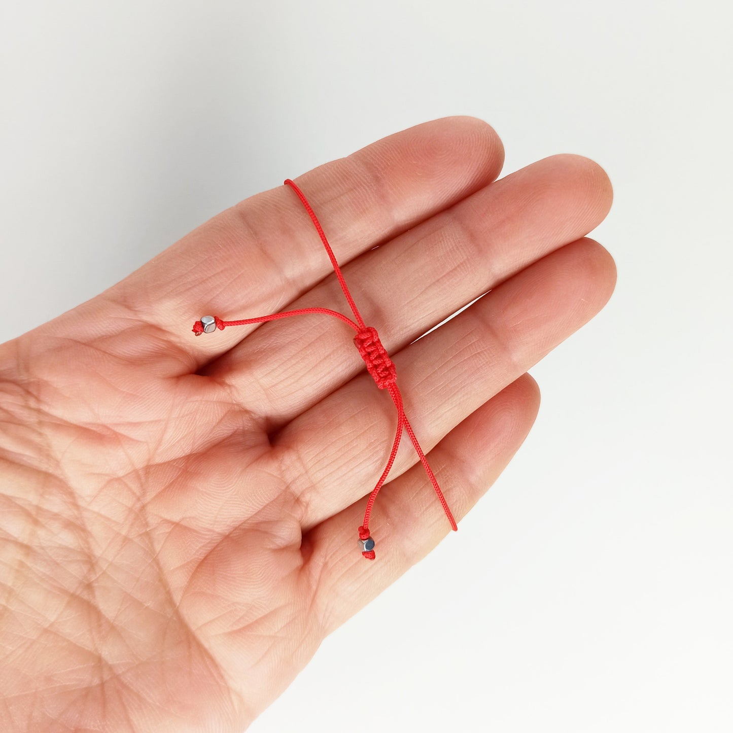 Esta es una pulsera ajustable elaborada en hilo rojo de 0.50 mm. Está hecha en 50% algodón y 50% poliéster. El nudo corredizo de macramé te permite ajustarla como más te guste.