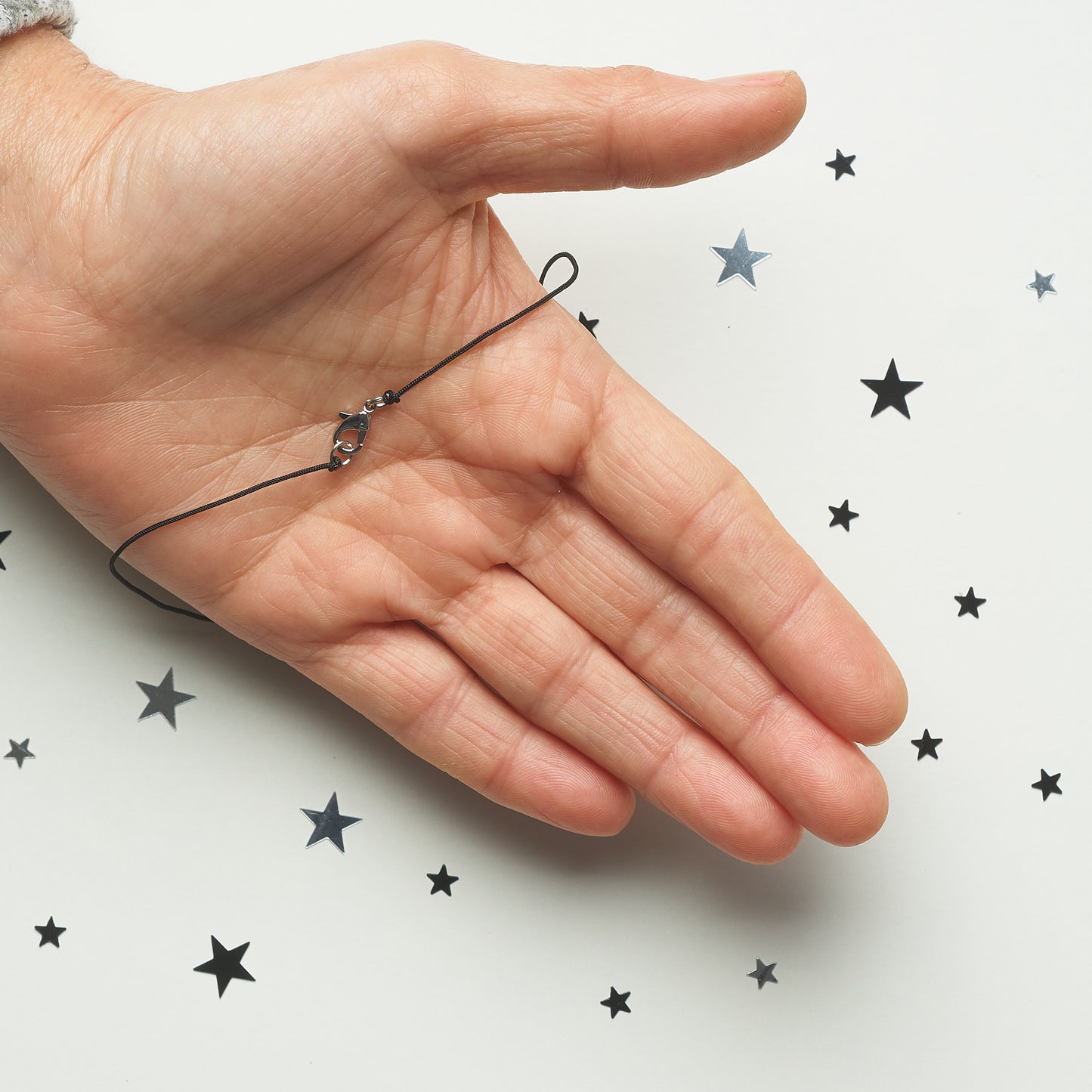 Mano sosteniendo un collar 7 chakras con piedras naturales sobre fondo blanco decorado con estrellas negras.