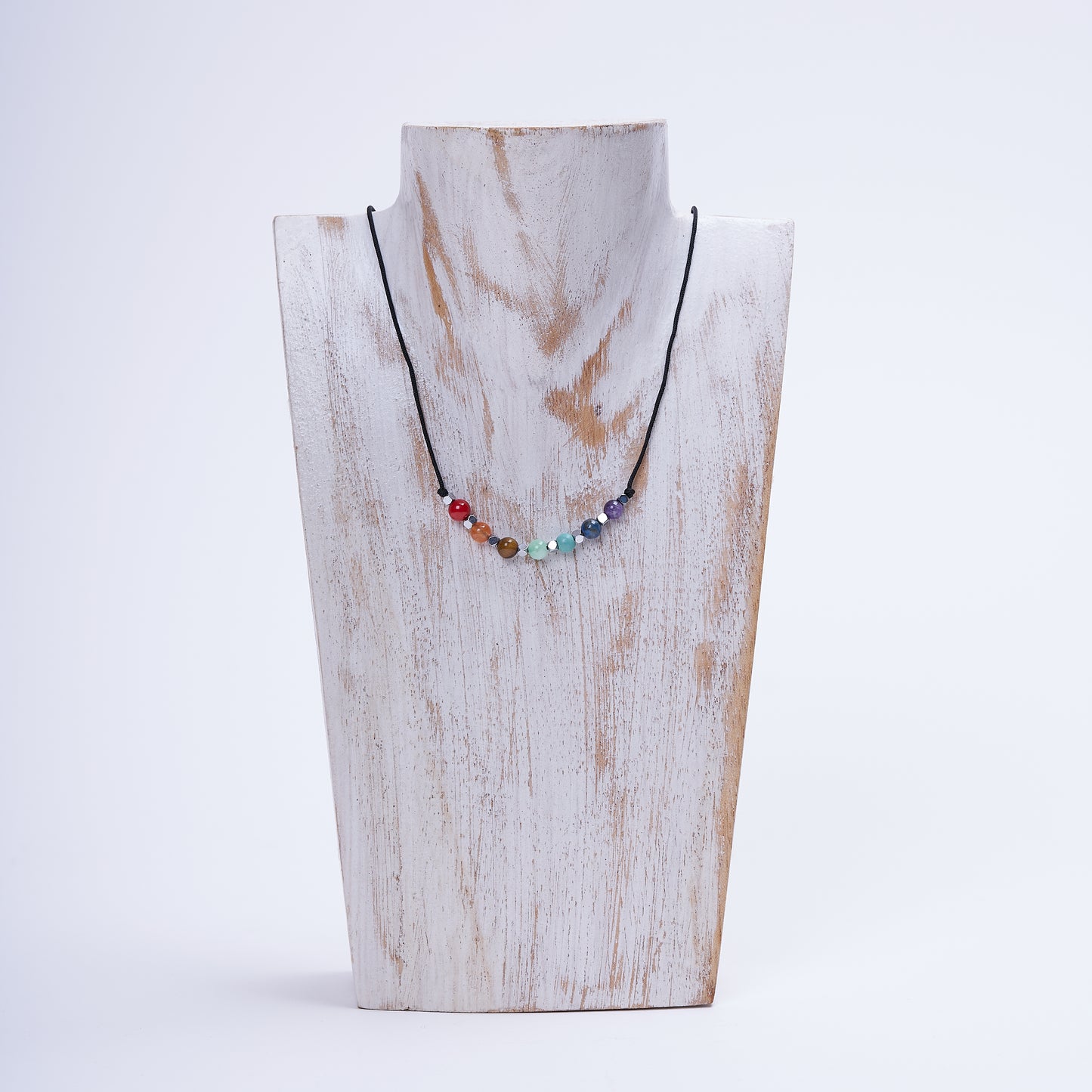 Collar de 7 chakras con cuentas de piedras naturales, exhibido en un soporte blanco texturizado sobre fondo claro.