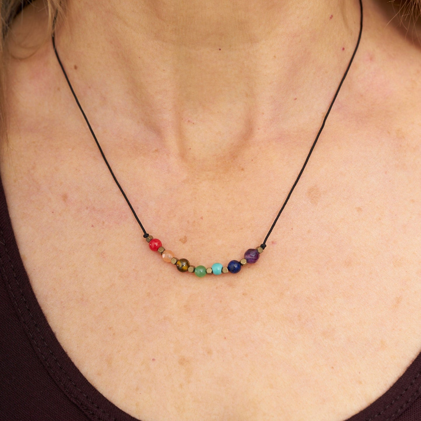 Collar con colgante de 7 piedras naturales que representan los chakras, sobre un cordón negro, usado alrededor del cuello.